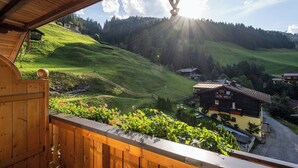 Un balcon en bois offrant une vue sur une colline verdoyante et sur un bâtiment à la façade jaune.