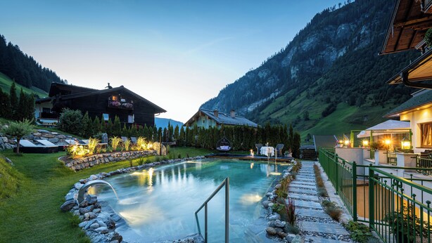 Un espace piscine bordé de pierres, doté d’une rambarde en métal et offrant une vue sur les montagnes en arrière-plan.