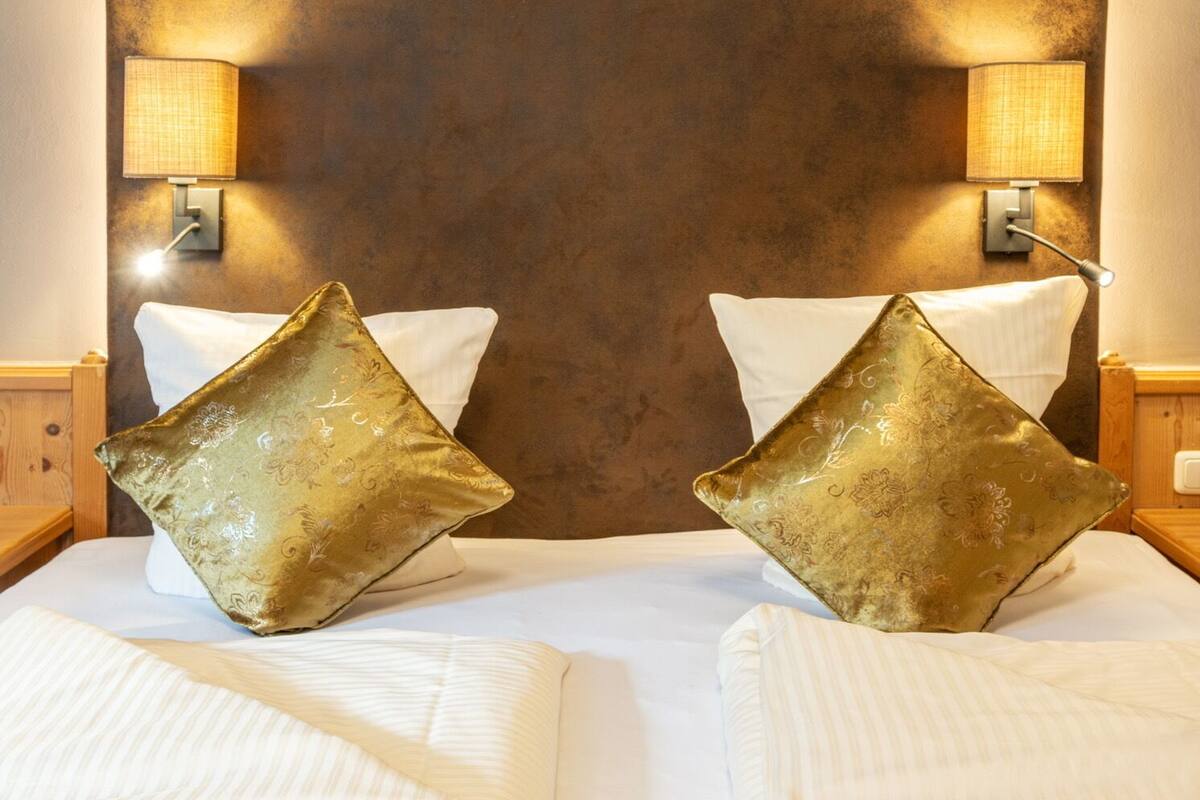 Ein Hotelzimmer mit einem großen Bett, zwei goldverzierenen Kissen und zwei Wandlampen.