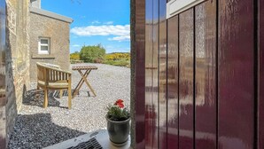 A rustic building with a gravel courtyard, a wooden bench, a table, and a potted plant. - Rowan Cottage - UK38991 (Dalcross)