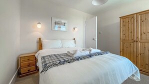 A neatly made bed with a checkered throw, a bedside table, a wooden wardrobe, and a framed picture on the wall. - Rowan Cottage - UK38991 (Dalcross)