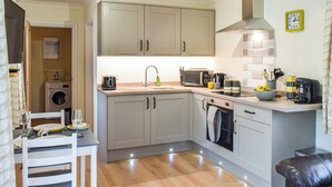 Cozinha compacta equipada com máquina de lavar, área de jantar com mesa e cadeiras, e sala de estar com sofá.