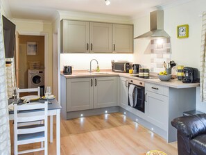 A compact kitchen with a washing machine, a dining area with a table and chairs, and a living area with a sofa. - 1 bedroom accommodation in Helston, near Helston and the Lizard Peninsula (Helston, near Helston and the Lizard Peninsula)