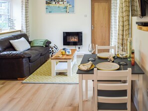 A cozy living room with a sofa, coffee table, and dining table set for two. A television is mounted on the wall, and a window with curtains is visible. - 1 bedroom accommodation in Helston, near Helston and the Lizard Peninsula (Helston, near Helston and the Lizard Peninsula)