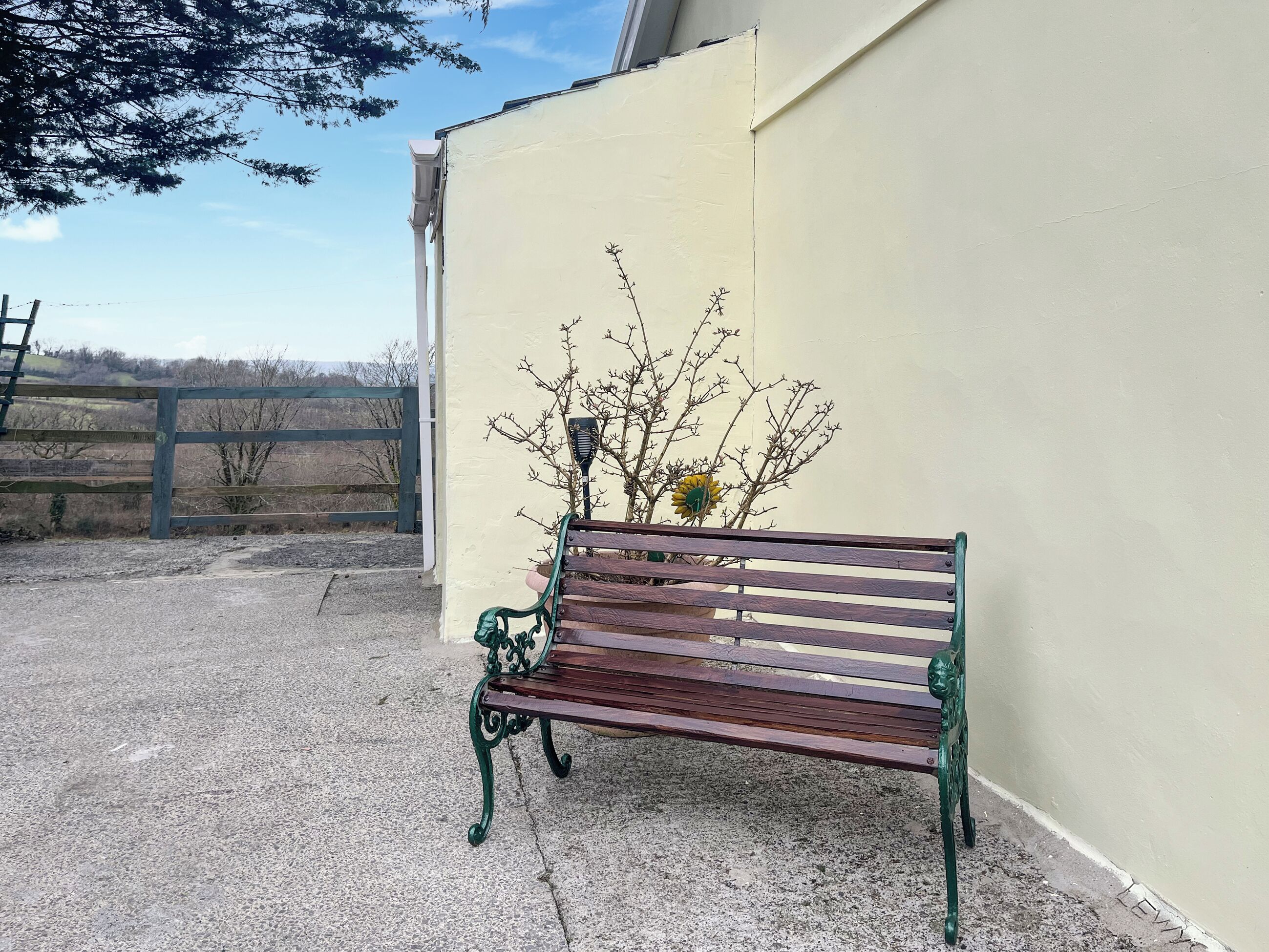 A bench outside a building with a plain wall and a fence in the background.