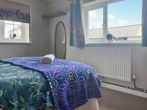 A bedroom with a bed covered in patterned blankets, a window with curtains, a radiator, and a wall-mounted mirror. - 1 bedroom accommodation in Llanarthney (Llanarthney)