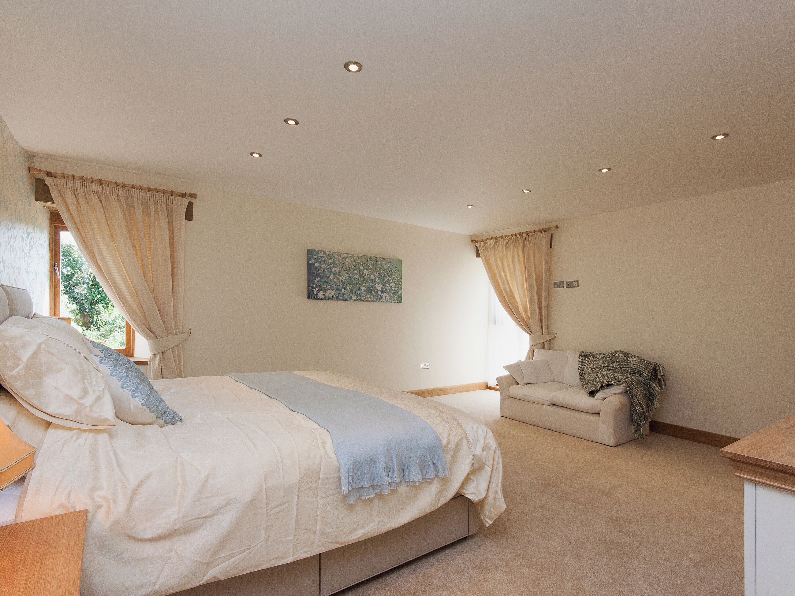 Een slaapkamer met een bed, een stoel, een schilderij en inbouwspots.