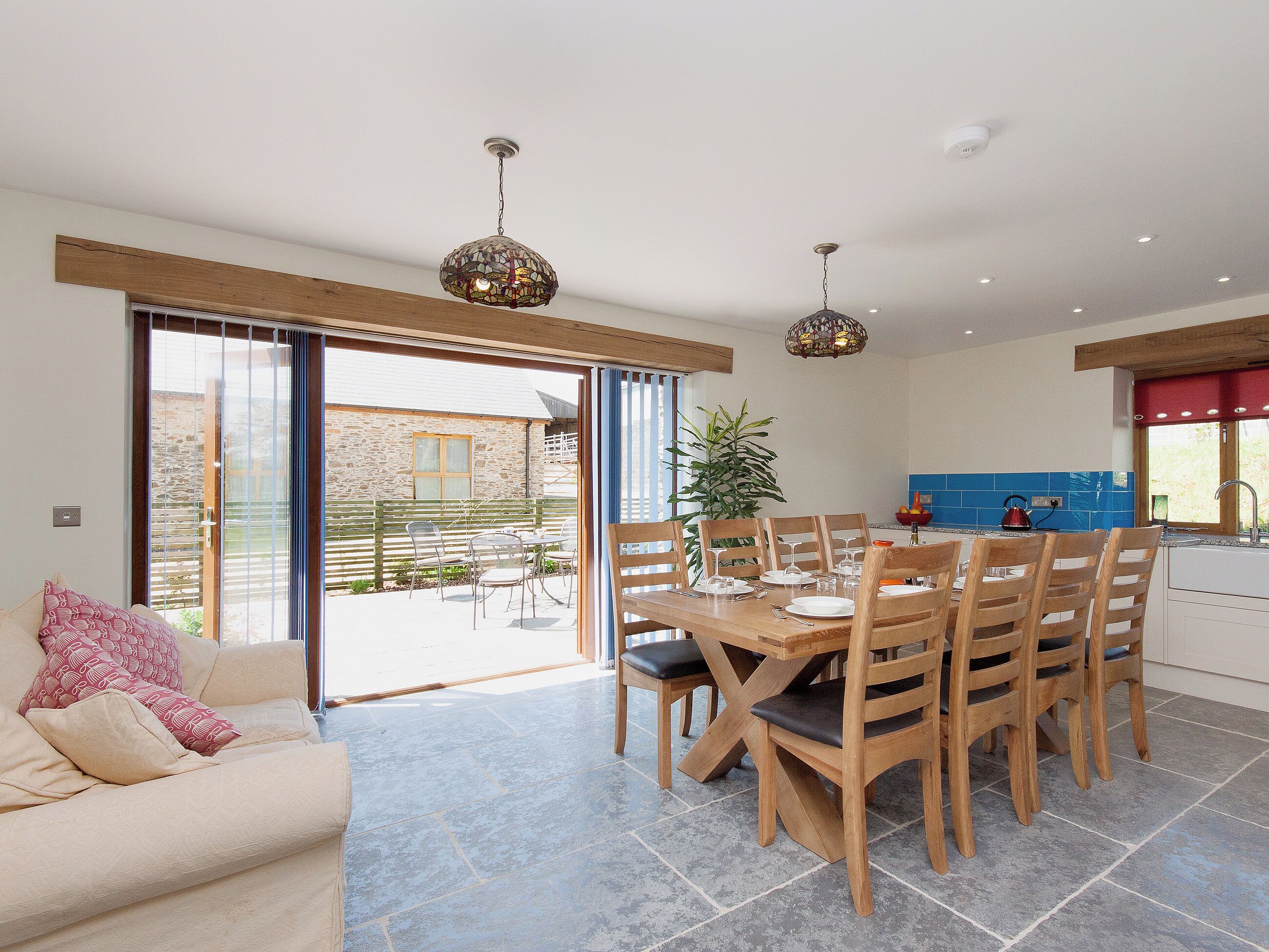 Un grand espace à manger avec une table et des chaises en bois, une cuisine aux carreaux bleus et une porte-fenêtre coulissante donnant sur un patio extérieur.