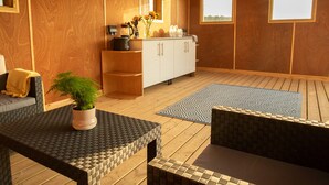 Une pièce aux murs en bois, avec un meuble blanc, une machine à café, une plante et un tapis à motifs.