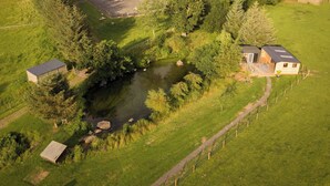 Vue aérienne d’une propriété rurale comprenant un étang, un enclos et une petite maison dotée d’une terrasse.