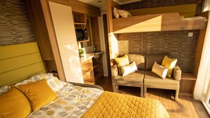 Une petite pièce comprenant un lit superposé, un canapé, un lit avec une literie à motifs et un four à micro-ondes posé sur une étagère.