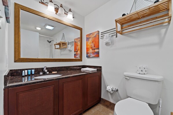 Un baño con un espejo grande, tocador de madera, inodoro blanco y dos cuadros en la pared.