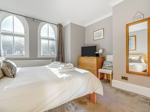 Quarto com cama, penteadeira, televisão, espelho e janelas grandes.