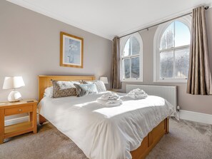 A hotel room with a large bed, a nightstand, a lamp, a framed picture on the wall, and a window with curtains. - Immaculate Sea View Apartment - Desirable West Cliff Location. (Whitby)