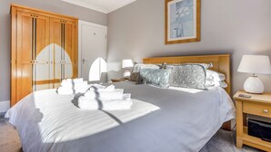 Habitación de hotel con una cama grande, un armario de madera, una mesita de noche con lámpara y un cuadro enmarcado en la pared.