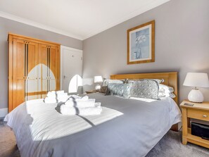 A hotel room with a large bed, a wooden wardrobe, a bedside table with a lamp, and a framed picture on the wall. - Immaculate Sea View Apartment - Desirable West Cliff Location. (Whitby)