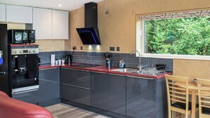 A modern kitchen with dark cabinets, a red countertop, a built-in oven, and a window with a view of greenery.