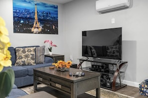 A modern living room with a sofa, coffee table, TV, and artwork.