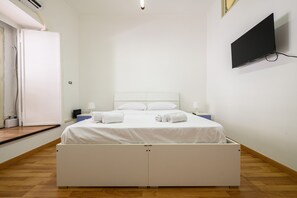 A bedroom with a bed, two bedside tables, a flat-screen TV, and a door.