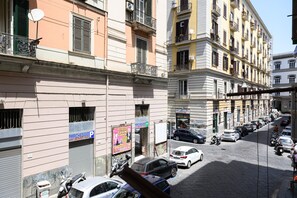 Gadesyn med parkerede biler, bygninger med balkoner og et skilt med teksten 'Piazza P'.