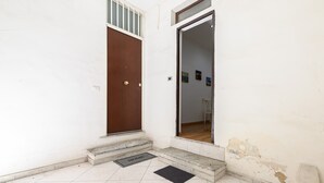 Une entrée aux murs blancs, dotée d’une porte en bois et d’une porte vitrée qui donne accès à l’intérieur.