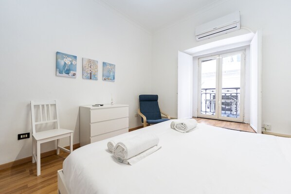 A hotel room with a bed, a chair, a desk, a balcony view, and three paintings on the wall.