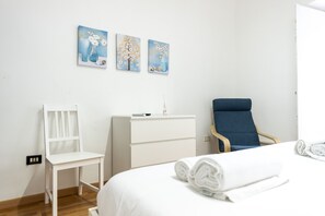 A hotel room with a bed, a white dresser, a blue chair, and three wall-mounted paintings.