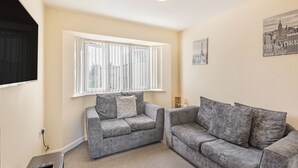 A living room with two grey sofas, a window with blinds, a ceiling light, and a wall-mounted picture of Paris and New York. - Rainbow Bungalow 1 - UK39809 (Chapel St Leonards)