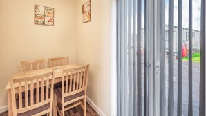 A dining area with a wooden table and chairs, a window with vertical blinds, and two wall-mounted signs. - Rainbow Bungalow 1 - UK39809 (Chapel St Leonards)