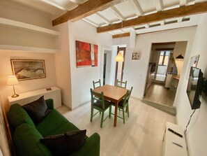 Een woonkamer met een groene bank, een houten eettafel en een keuken op de achtergrond.