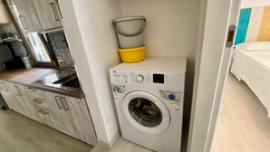 Une petite buanderie équipée d’un lave-linge, d’un évier jaune et d’un autre évier.