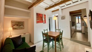 Un coin repas avec une table et des chaises en bois, un canapé vert, un tableau et une horloge au mur.