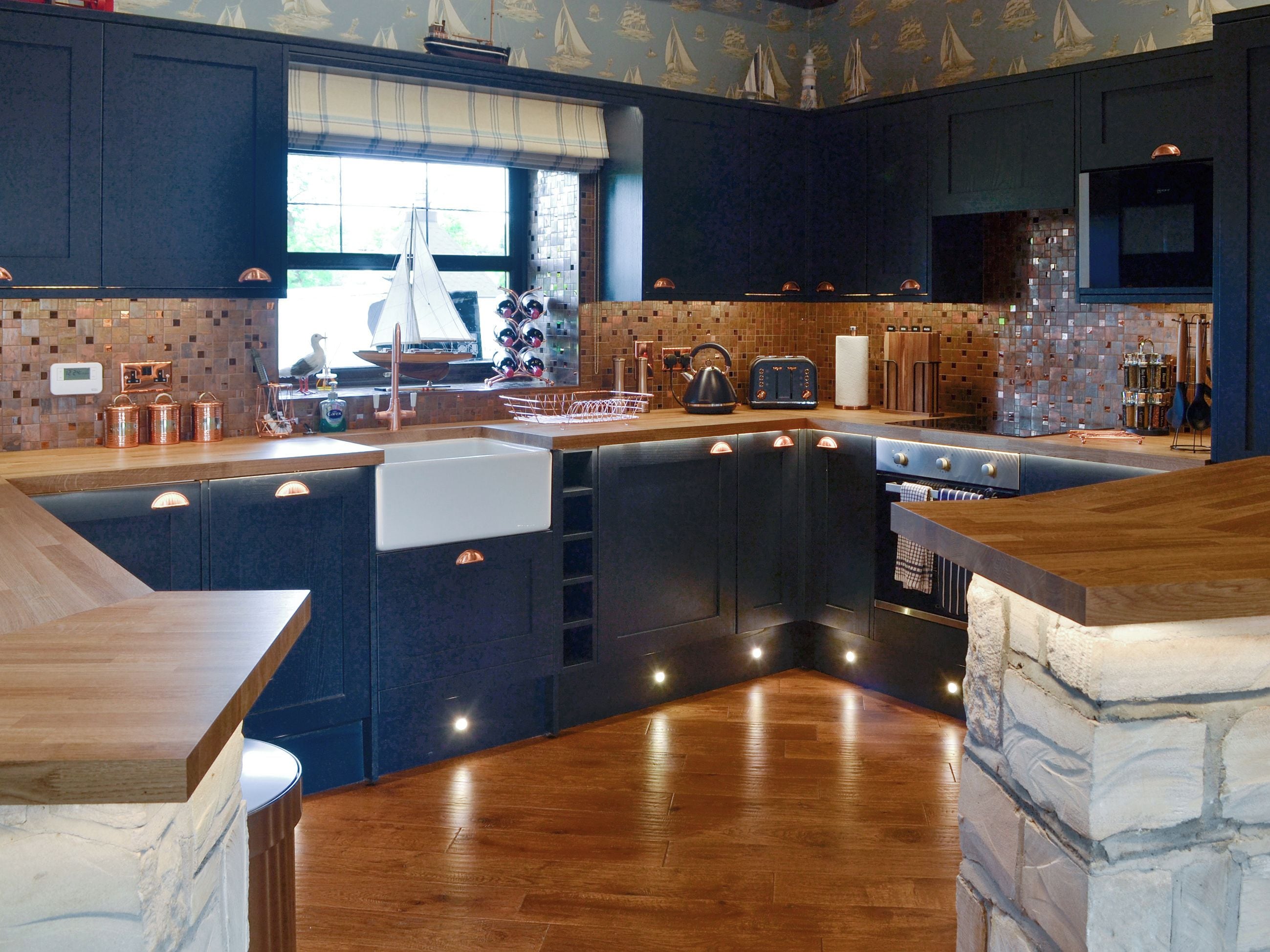A modern kitchen with a central island, dark cabinetry, and a wooden floor.