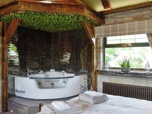 A spa area with a hot tub, wooden beams, a brick wall, and a window with a view.