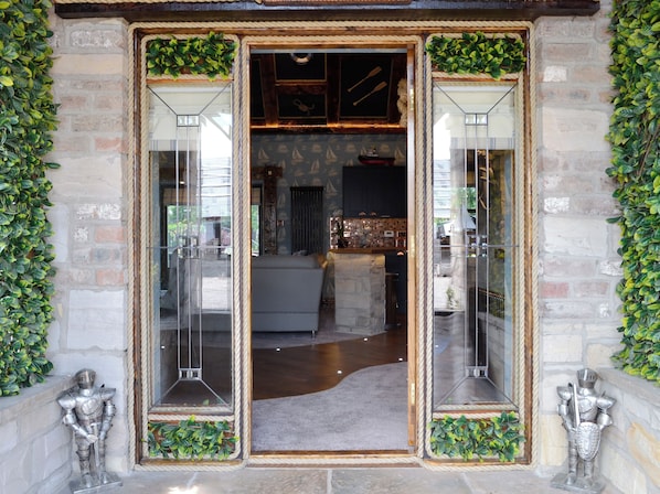 A stone facade with a glass door entrance, a visible kitchen area with a dining table, and a statue of a knight.