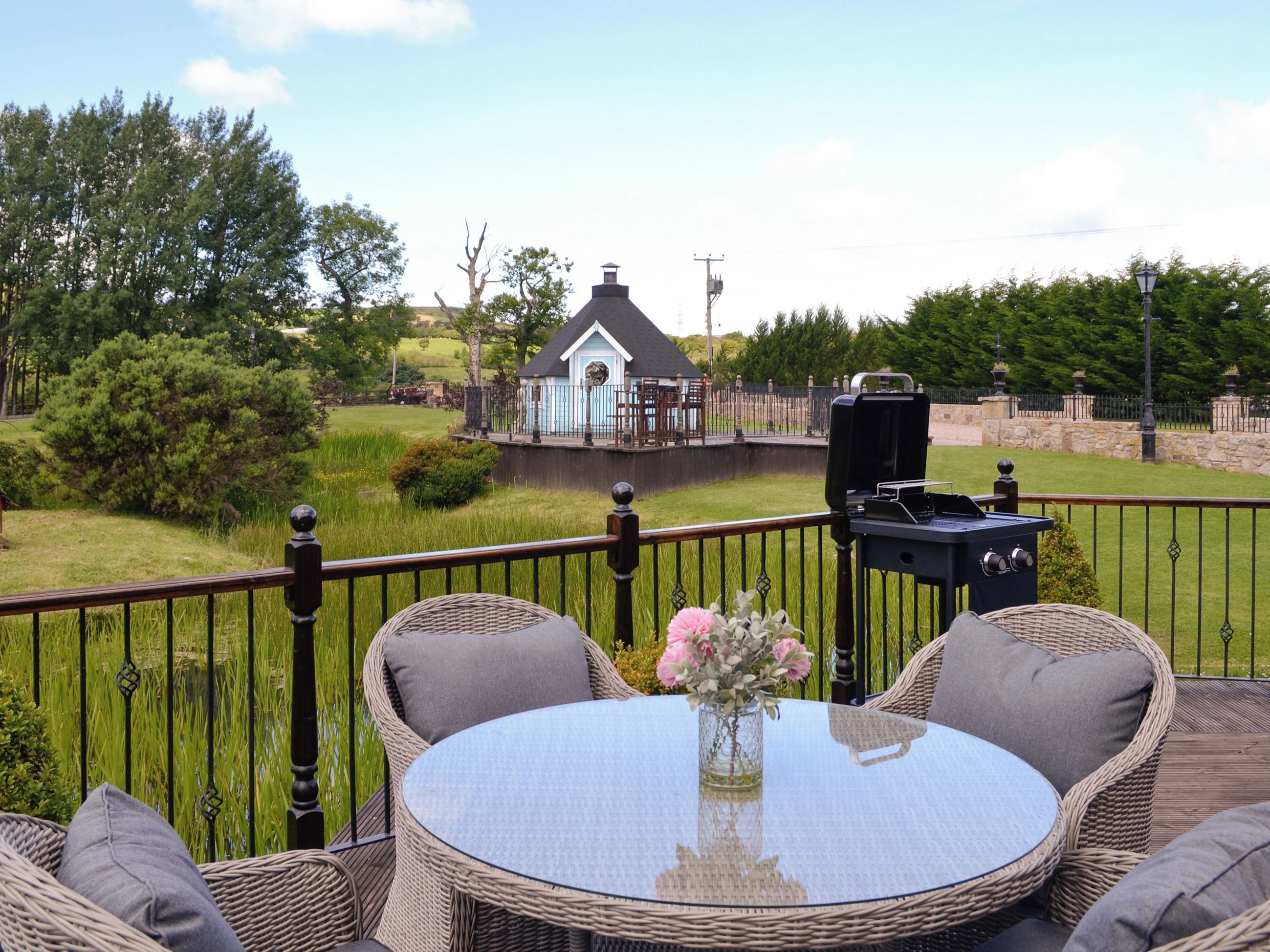 A deck with wicker furniture, a glass table, and a grill.