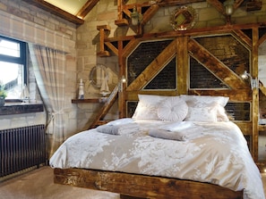 A rustic bedroom with exposed wooden beams, a stone wall, a bed with floral bedding, and nautical decor.