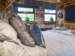 Un dormitorio rústico con pared de piedra, cama con ropa de cama floral y ventana con vistas al verdor.