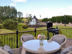 Eine Terrasse mit Korbmöbeln, einem Glastisch und einem Grill.
