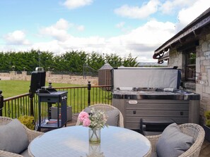 Un patio al aire libre con una mesa redonda, sillas de mimbre, una parrilla y un jacuzzi.