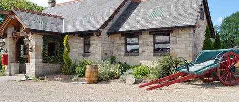 A stone building with a sloped roof, a small porch, and a carriage in front.