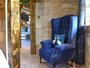 A room with a stone wall, a blue upholstered armchair with a decorative pillow, and a wooden door.