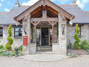 A stone building with a wooden porch, a red mailbox, and two tall, narrow trees.