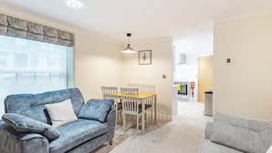A living room with a sofa, a dining table with chairs, a kitchen area with a stove, and a door leading to another room. - Salem Porter- UK34814 (Wainfleet, near Skegness)