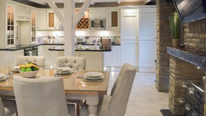 Een moderne keuken met witte kasten, een eethoek met een glazen tafel en een stenen openhaard.