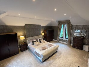 Ein Schlafzimmer mit einem großen Bett, zwei Nachttischen, einem Kleiderschrank und einem Fenster mit Vorhängen.