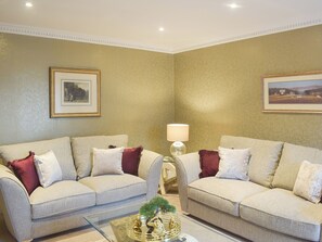 A living room with two sofas, a glass coffee table, a lamp, and framed pictures on the walls.