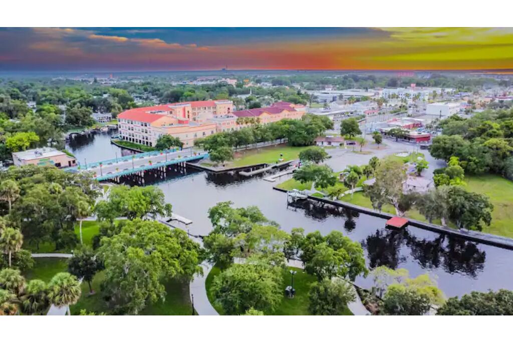 An aerial view of a city with a prominent red-roofed building, a bridge, and a river.