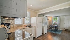 A compact kitchen with a built-in stove, white cabinets, and a dining area with a table and chairs. - East Riverside Downtown Bungalow (Port Richey)