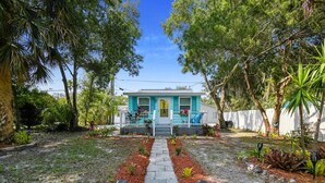 A turquoise house with a front porch, surrounded by a garden with a stone pathway leading to the entrance. - East Riverside Downtown Bungalow (Port Richey)
